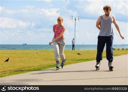 Love romance leisure outdoor fitness sport concept. Young pair riding rollerskates in park. Girl and boy together on skates.. Young pair riding rollerblades in park.