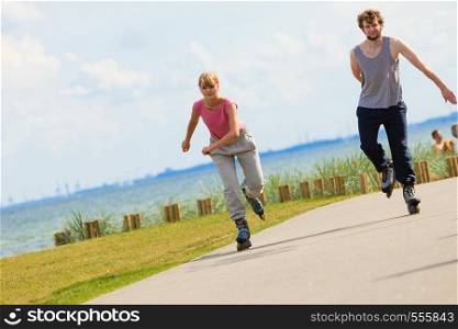 Love romance sport fitness leisure concept. Teen couple together on skates. Girl and boy riding rollerskates in coastal park.. Teen couple together on skates.