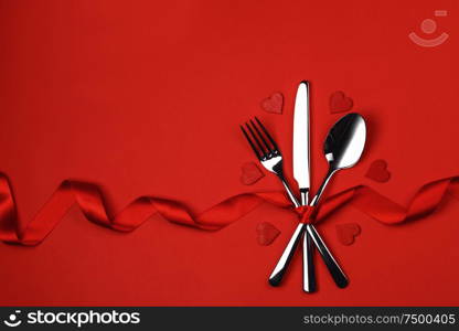 Love, romance, Valentine&rsquo;s day concept - festive table setting cutlery and decorative hearts on red background. Table setting cutlery on red