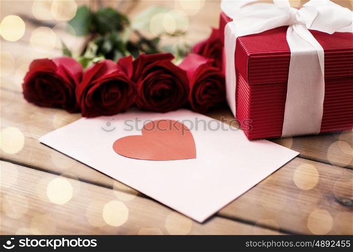 love, romance, valentines day and holidays concept - close up of gift box, red roses and greeting card with heart on wood (vintage effect)