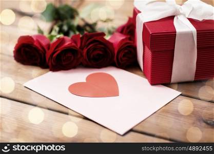 love, romance, valentines day and holidays concept - close up of gift box, red roses and greeting card with heart on wood (vintage effect)
