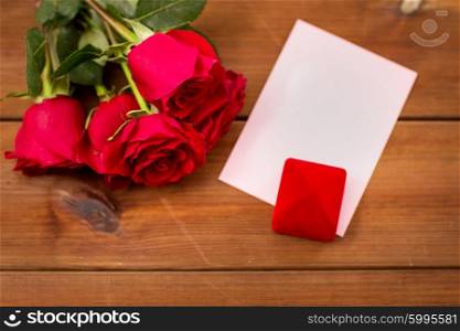 love, romance, valentines day and holidays concept - close up of gift box, red roses and greeting card on wood