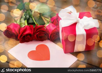 love, romance, valentines day and holidays concept - close up of gift box, red roses and greeting card with heart on wood