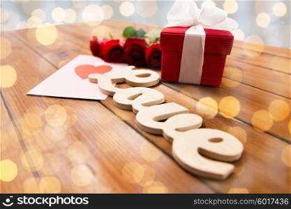 love, romance, valentines day and holidays concept - close up of gift box, red roses and greeting card with heart on wood over lights background