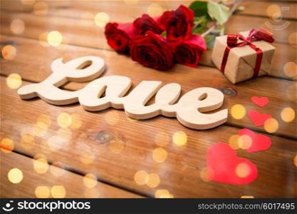 love, romance, valentines day and holidays concept - close up of gift box, red roses and hearts on wood over lights background