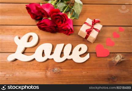 love, romance, valentines day and holidays concept - close up of gift box, red roses and hearts on wood