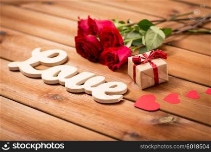 love, romance, valentines day and holidays concept - close up of gift box, red roses and hearts on wood
