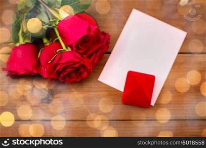 love, romance, valentines day and holidays concept - close up of gift box, red roses and greeting card on wood