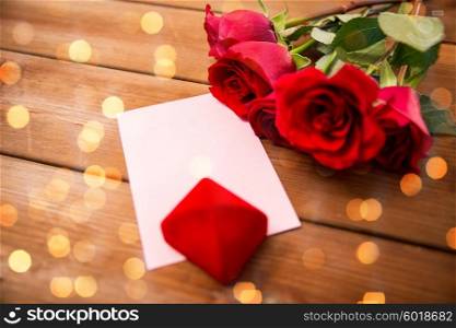 love, romance, valentines day and holidays concept - close up of gift box, red roses and greeting card with heart on wood over lights background