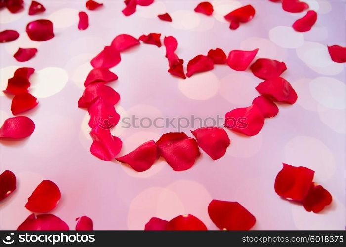 love, romance, valentines day and holidays concept - close up of red rose petals in heart shape over pink background