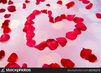 love, romance, valentines day and holidays concept - close up of red rose petals in heart shape over pink background