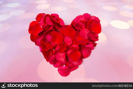 love, romance, valentines day and holidays concept - close up of red rose petals in heart shape over pink background