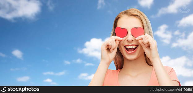 love, romance, valentines day and people concept - smiling young woman or teenage girl with red heart shapes on eyes over blue sky and clouds background