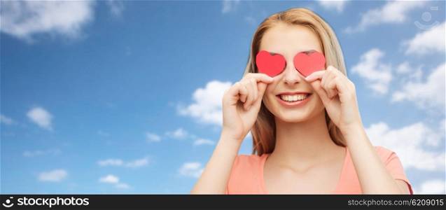 love, romance, valentines day and people concept - smiling young woman or teenage girl with red heart shapes on eyes over blue sky and clouds background