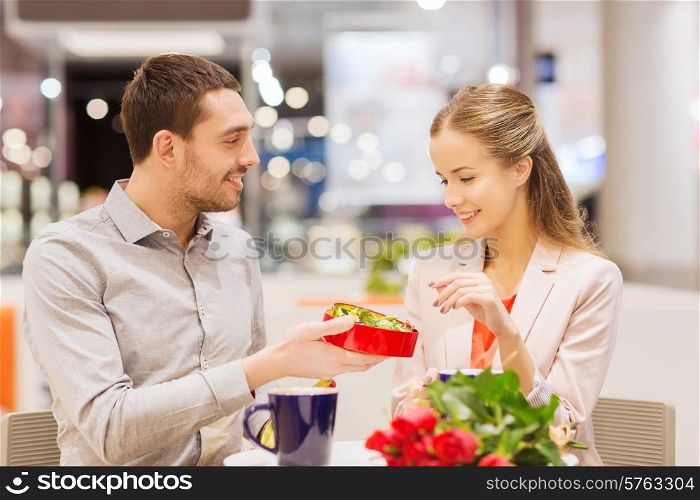love, romance, valentines day, couple and people concept - happy young couple with red flowers and open gift box in at cafe mall