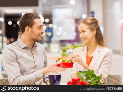 love, romance, valentines day, couple and people concept - happy young couple with red flowers and open gift box in at cafe mall