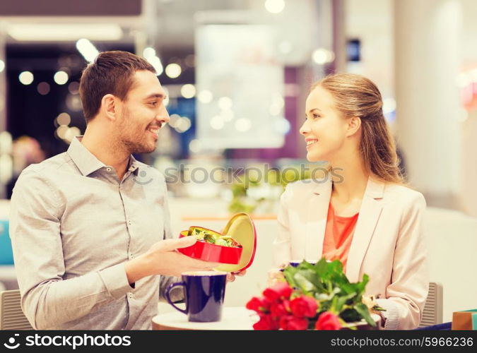 love, romance, valentines day, couple and people concept - happy young couple with red flowers and open gift box in at cafe mall