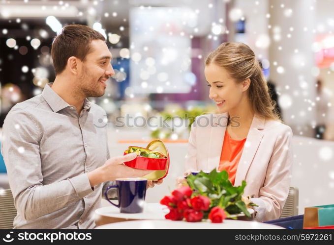 love, romance, valentines day, couple and people concept - happy young couple with red flowers and open gift box in at cafe mall with snow effect