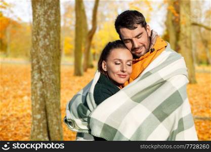 love, season and people concept - happy smiling couple in warm blanket over autumn park background. happy couple in warm blanket over autumn park