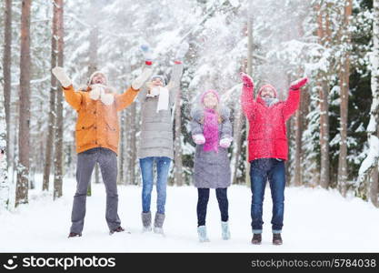 love, season, friendship and people concept - group of happy men and women having fun and playing with snow in winter forest