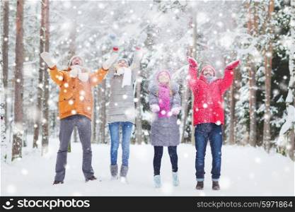 love, season, friendship and people concept - group of happy men and women having fun and playing with snow in winter forest