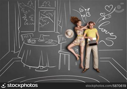 Love story concept of a romantic couple against chalk drawings background. Male listening to the music in the headphones and surfing internet via laptop, female trying to gain his attention.