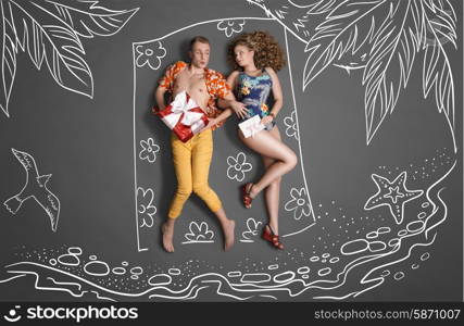 Love story concept of a romantic couple against chalk drawings background. Young couple on vacation, lying on the beach and sharing gifts.