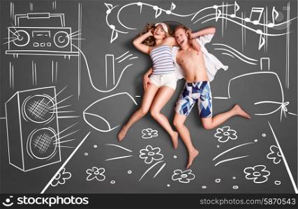 Love story concept of a romantic couple lying in bed, sharing headphones, and listening to the music against chalk drawings background of a bedroom with acoustic system.