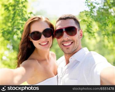 love, summer and people concept - smiling couple wearing sunglasses making selfie over green natural background. smiling couple wearing sunglasses making selfie. smiling couple wearing sunglasses making selfie