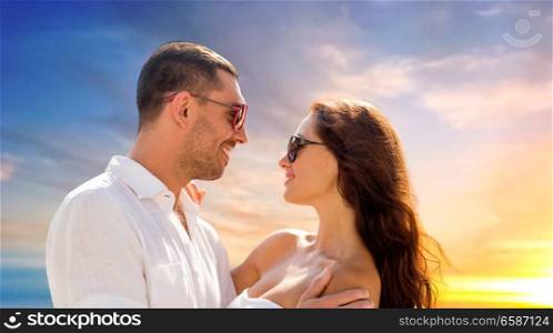 love, summer and relationships concept - happy smiling couple in sunglasses hugging over evening sky background. happy smiling couple in sunglasses hugging