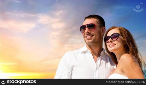 love, summer and relationships concept - happy smiling couple in sunglasses over evening sky background. happy smiling couple in sunglasses