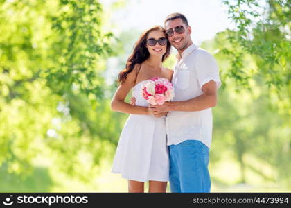 love, summer and relationships concept - happy smiling couple with bunch of flowers hugging over green natural background. happy couple with bunch of flowers hugging. happy couple with bunch of flowers hugging