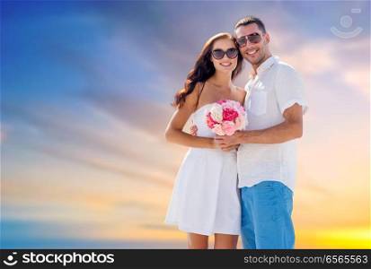 love, summer and relationships concept - happy smiling couple with bunch of flowers hugging over evening sky background. happy couple with bunch of flowers hugging