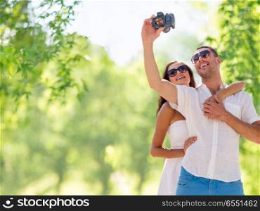 love, summer and technology concept - smiling couple in sunglasses making selfie by digital camera over green natural background. smiling couple making selfie by digital camera. smiling couple making selfie by digital camera