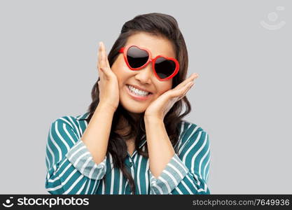 love, summer and valentines day concept - happy asian young woman in heart shaped sunglasses over grey background. happy asian woman with in heart shaped sunglasses