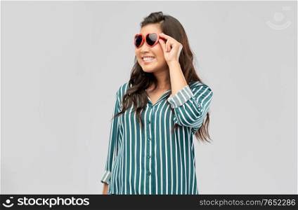 love, summer and valentines day concept - happy asian young woman in heart shaped sunglasses over grey background. happy asian woman with in heart shaped sunglasses