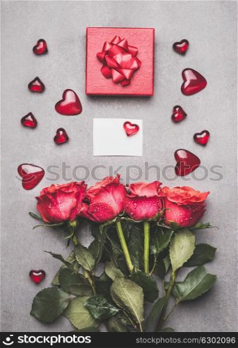 Love symbols composing with red gift box, ribbon, roses bunch , blank white paper card and heart, top view. Mock up for greeting for Mothers day,birthday or Valentine?s Day