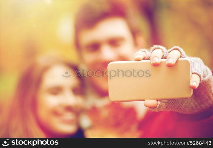 love, technology, relationship, family and people concept - happy couple taking selfie by smartphone in autumn park. couple taking selfie by smartphone in autumn park