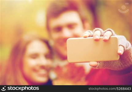 love, technology, relationship, family and people concept - happy couple taking selfie by smartphone in autumn park. couple taking selfie by smartphone in autumn park