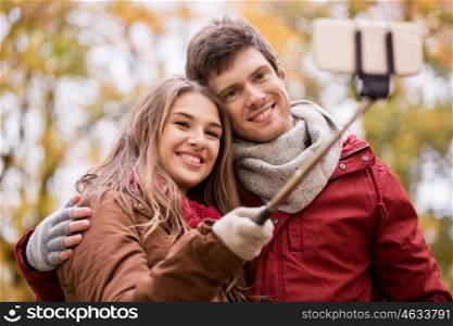 love, technology, relationship, family and people concept - happy smiling couple taking picture by smartphone selfie stick in autumn park