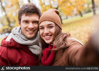 love, technology, relationship, family and people concept - happy smiling young couple taking selfie in autumn park