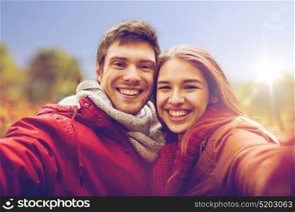 love, technology, relationship, family and people concept - happy smiling young couple taking selfie in autumn park. happy young couple taking selfie in autumn park
