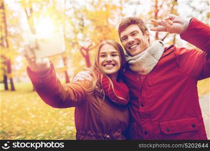 love, technology, relationship, family and people concept - smiling couple taking selfie by smartphone in autumn park. couple taking selfie by smartphone in autumn park