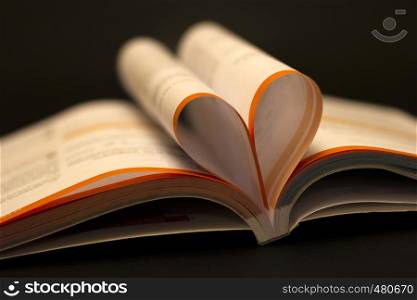 Love to read a book concept. Open book with heart shape page on black table. Education background, back to school concept.