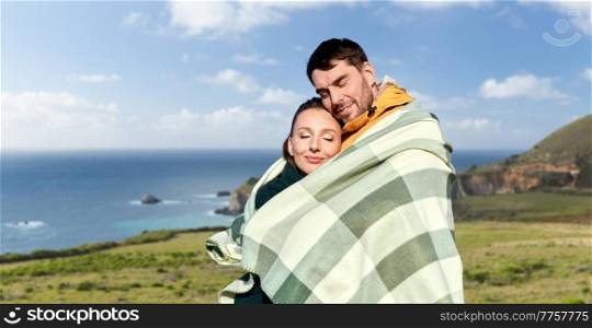love, travel and tourism concept - happy smiling couple in warm blanket over big sur coast of california background. happy couple in warm blanket in california