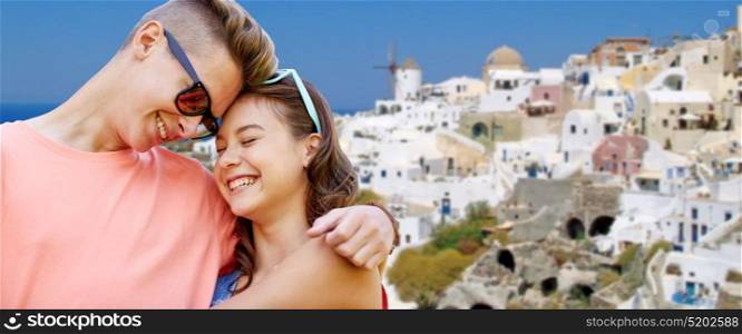love, travel, tourism and people concept - happy smiling teenage couple hugging over oia town on santorini island background. happy teenage couple hugging on santorini island