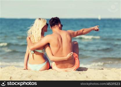 love, travel, tourism and people concept - smiling couple on vacation in swimwear sitting, hugging and pointing finger on summer beach from back