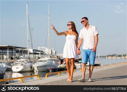 love, travel, tourism and people concept - smiling couple wearing sunglasses walking at harbor and pointing finger