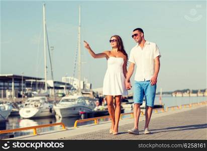 love, travel, tourism and people concept - smiling couple wearing sunglasses walking at harbor and pointing finger