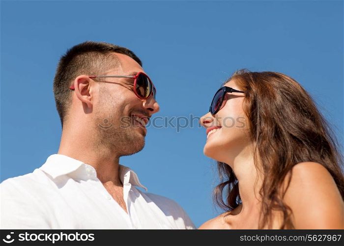 love, travel, tourism, people and friendship concept - smiling couple wearing sunglasses looking at each over blue sky background